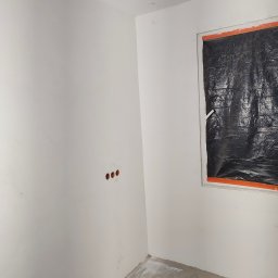 MIX MIR USŁUGI REMONTOWO WYKOŃCZENIOWE MIROSŁAW KALINKA - Pokój w trakcie przygotowań do malowania: okno zabezpieczone folią, ściany zagruntowane, widoczne puszki instalacyjne elektryczne.