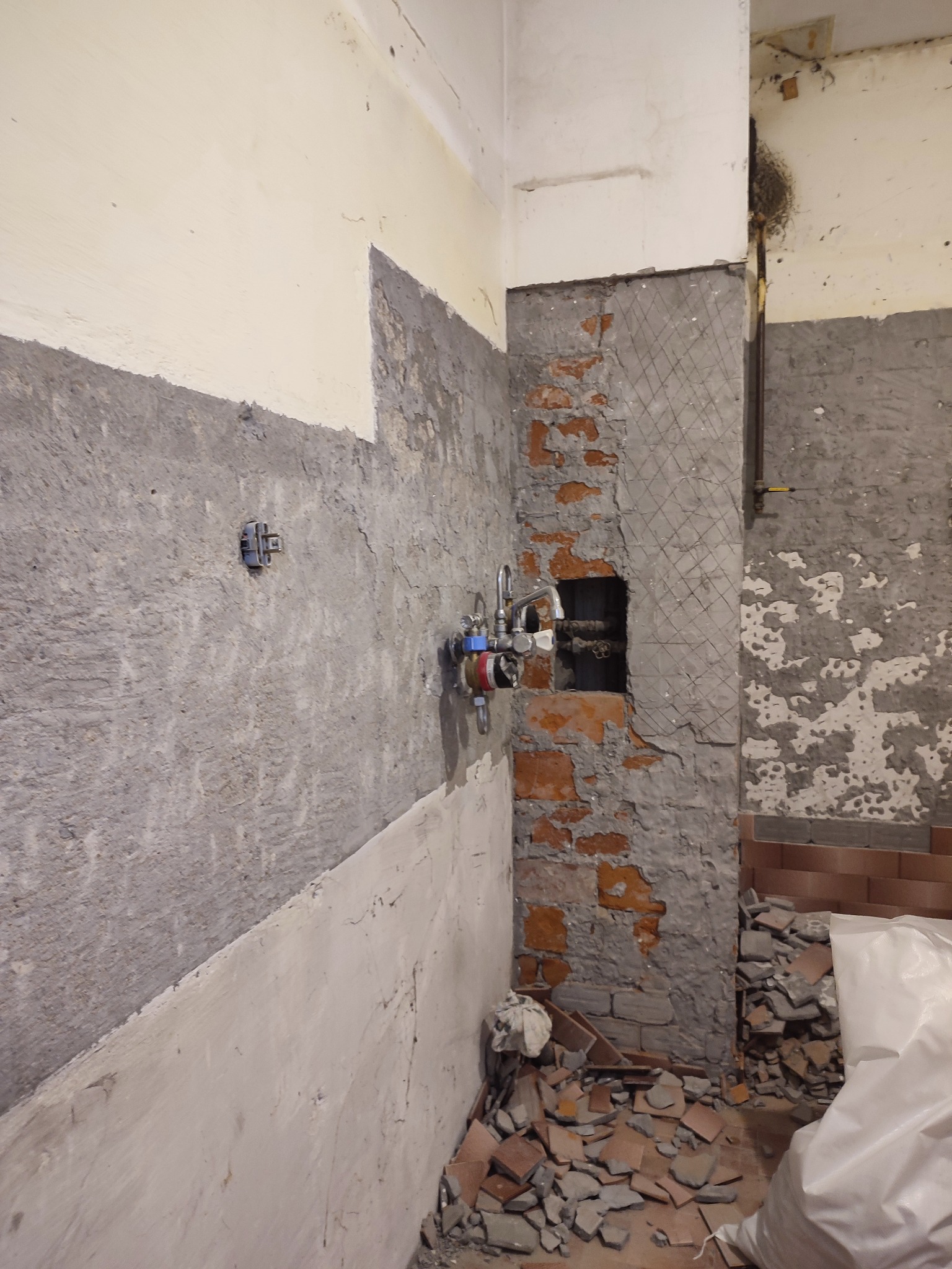 Demontaż płytek i przygotowanie ścian do remontu łazienki, widoczne odsłonięte cegły, instalacja wodna i fragmenty starych płytek na podłodze.