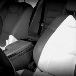 Wnętrze samochodu z jasną skórzaną tapicerką, widoczny fotel kierowcy i pasażera, oświetlone przez silne światło słoneczne padające na siedzenie.