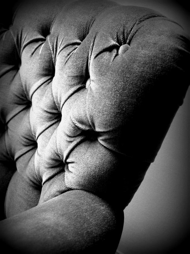 Fragment ciemnoszarej, pikowanej kanapy z głębokimi wciągnięciami i guzikami, sfotografowany z bliska w czerni i bieli.