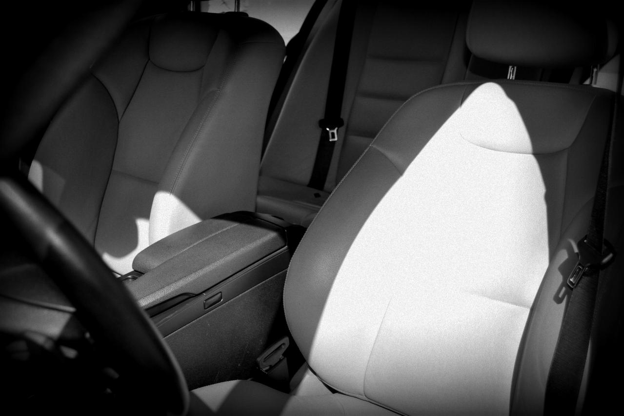 Wnętrze samochodu z jasną skórzaną tapicerką, widoczny fotel kierowcy i pasażera, oświetlone przez silne światło słoneczne padające na siedzenie.