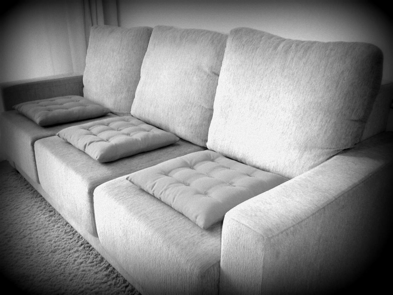 Czarno-białe zdjęcie trzyosobowej sofy z jasną tapicerką i trzema poduszkami siedziskowymi z pikowaniem, ustawionej na dywanie.