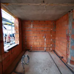 Surowy stan pomieszczenia z cegły z widocznymi przewodami elektrycznymi w ścianach i na podłodze, przygotowane punkty oświetleniowe na ścianach i suficie.