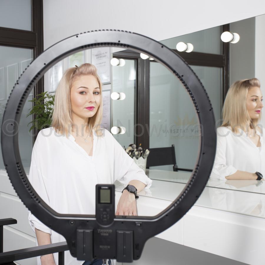 Portret blondynki z różowymi ustami, pozującej w studiu w oświetleniu ring light, z odbiciem w lustrze otoczonym żarówkami.