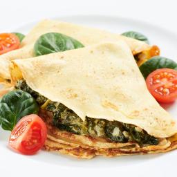 Restauracja Karpielówka - Delikatne naleśniki wypełnione szpinakiem i cebulą, udekorowane świeżymi liśćmi szpinaku i połówkami pomidorków koktajlowych na białym talerzu.