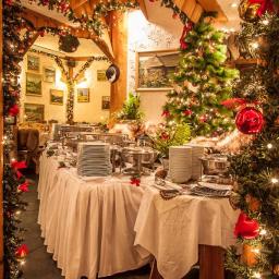 Restauracja Karpielówka - Świątecznie udekorowany stół bufetowy z podgrzewaczami i stosami talerzy w rustykalnej restauracji, ozdobiony choinkami i lampkami.