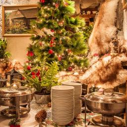 Restauracja Karpielówka - Uroczysty stół szwedzki z dekoracjami świątecznymi, w tle choinka i futrzana dekoracja, zastawa stołowa i podgrzewacze potraw.