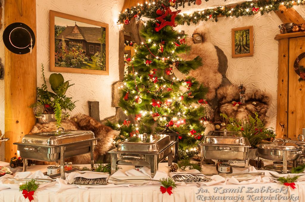 Świąteczny bufet z podgrzewaczami potraw w rustykalnej restauracji, w tle choinka i dekoracje, widoczne logo fotografa.
