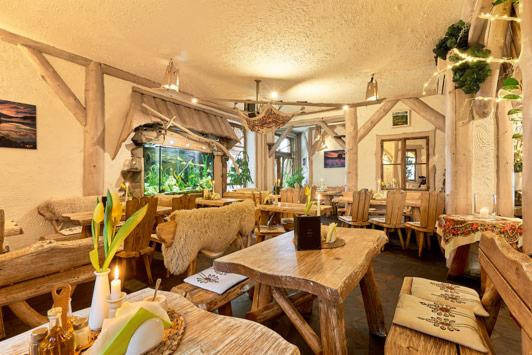 Rustykalne wnętrze restauracji z drewnianymi meblami, akwarium w ścianie i dekoracjami z naturalnych materiałów, oświetlone ciepłym światłem