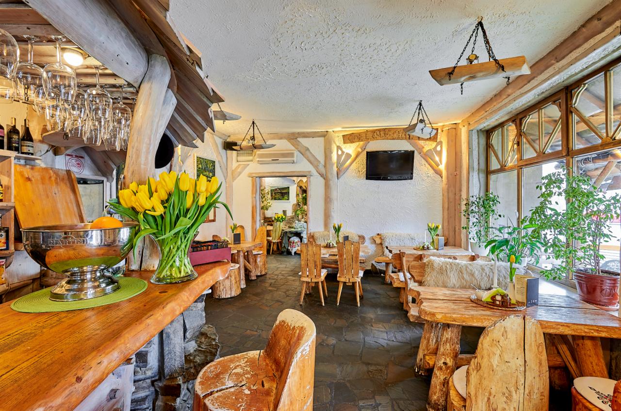 Rustykalne wnętrze restauracji z drewnianymi meblami, żółtymi tulipanami w wazonie na barze i ozdobnymi lampami wiszącymi.