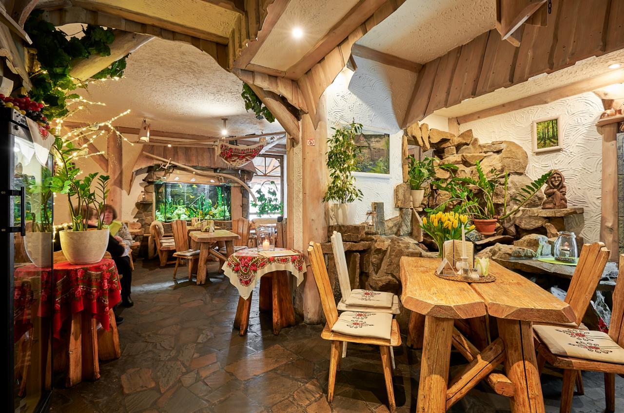Wnętrze restauracji z wystrojem w stylu rustykalnym: drewniane meble, kamienne elementy dekoracyjne, akwarium i rośliny doniczkowe.