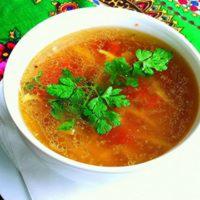 Aromatyczny rosół z warzywami i świeżą natką pietruszki, serwowany w białej miseczce w Warszawie. W tle kolorowa chusta ludowa.