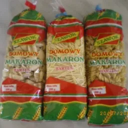 Trzy przezroczyste opakowania makaronu 'Domowy Makaron Bartos' o różnej gramaturze i kształtach: muszelki, nitki i świderki, ustawione obok siebie na jasnym tle.