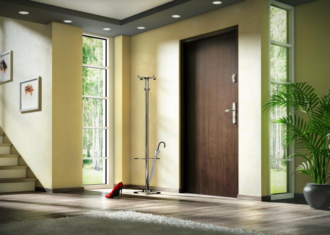 Wnętrze przedpokoju z brązowymi drzwiami wejściowymi, jasnymi ścianami, oknem z widokiem na zieleń, stojakiem na parasole i czerwonym szpilką obok, całość doświetlona punktowymi lampami sufitowymi.