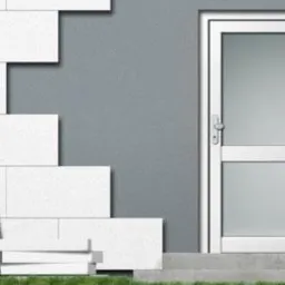 Ocieplanie ściany zewnętrznej białymi płytami styropianowymi, widoczna biała stolarka drzwiowa.