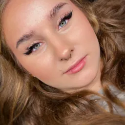 Portret młodej kobiety z profesjonalnie przedłużonymi rzęsami w stylu anime, delikatnym różem na policzkach i kolczykiem w nosie typu septum, leżącej na czarnym tle.