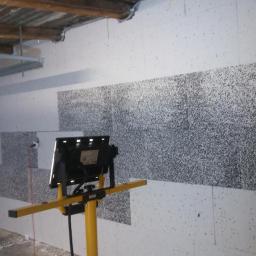 Bakis - Docieplanie ściany garażu styropianem grafitowym, widoczna lampa budowlana na statywie oświetlająca fragment ściany.