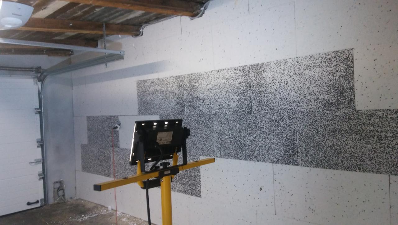 Docieplanie ściany garażu styropianem grafitowym, widoczna lampa budowlana na statywie oświetlająca fragment ściany.