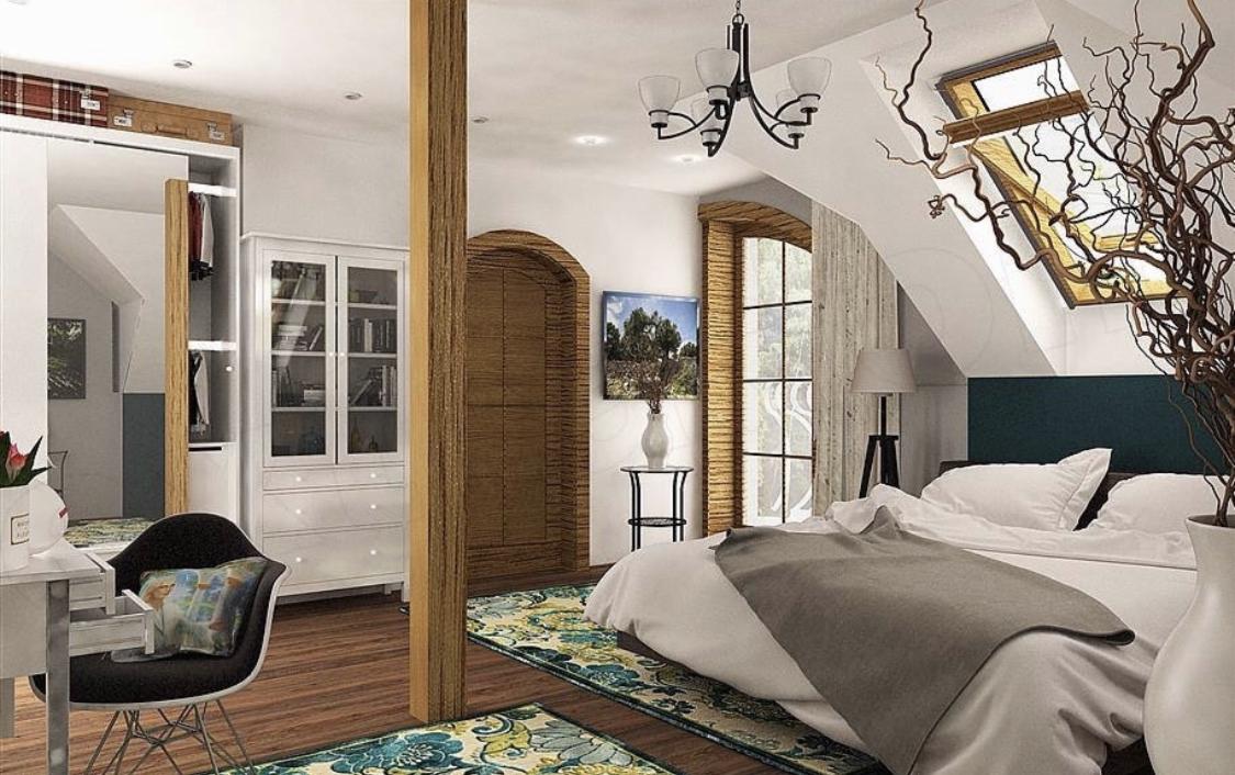 Jasna sypialnia na poddaszu z drewnianymi elementami, dużym łóżkiem, oknem dachowym i dekoracyjnymi gałęziami w wazonie.