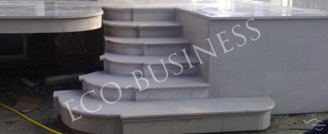 Zewnętrzne schody kamienne z zaokrąglonymi krawędziami stopni, prowadzące do tarasu, wykonane z jasnego marmuru.