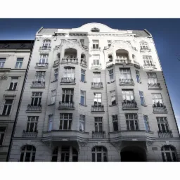 Elewacja odnowionej, secesyjnej kamienicy z balkonami i arkadami, widziana z dołu pod kątem, z fragmentem sąsiedniego budynku i latarnią uliczną.