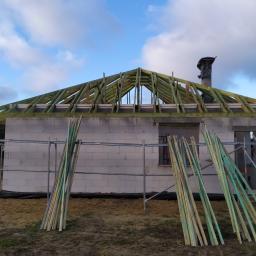 Usługi Budowlane Bartosz Ziółczyk - Budowa domu z białych bloczków: widoczna konstrukcja drewniana dachu, rusztowania i stos desek obok budynku.