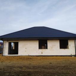 Usługi Budowlane Bartosz Ziółczyk - Surowy stan domu jednorodzinnego z białego bloczka, z zamontowanym, ciemnym dachem z dachówki ceramicznej, przygotowany do dalszych prac wykończeniowych, widoczne otwory okienne bez stolarki.