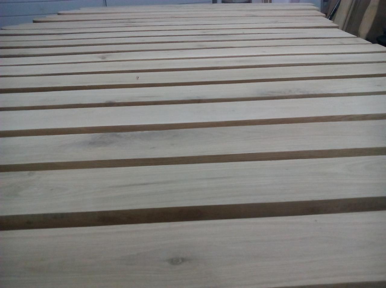 Surowe, jasne deski ułożone równolegle, prawdopodobnie przygotowane do budowy konstrukcji drewnianej.