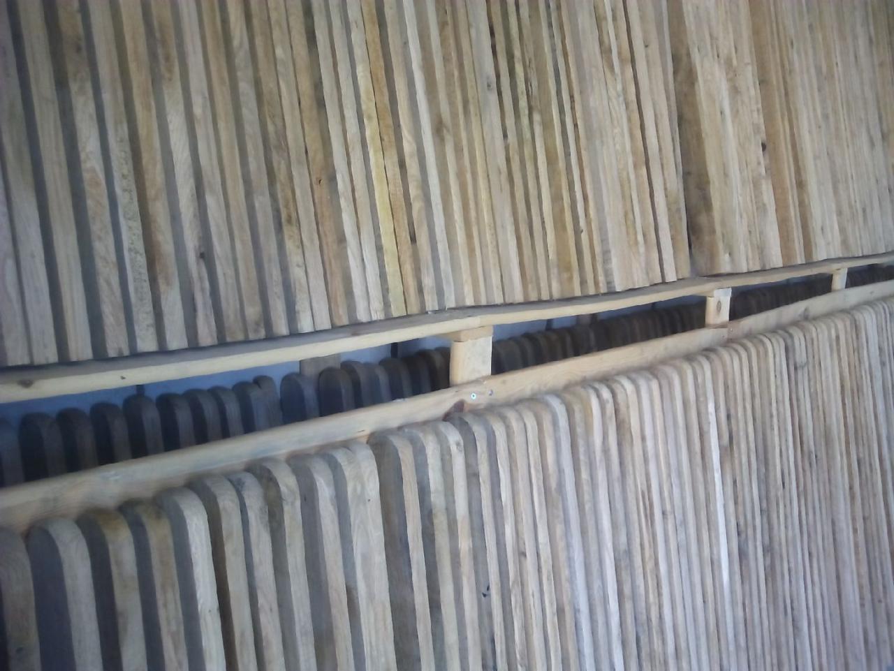 Surowe, pionowo ułożone deski z jasnego drewna, przygotowane do budowy konstrukcji, wsparte na drewnianych belkach.