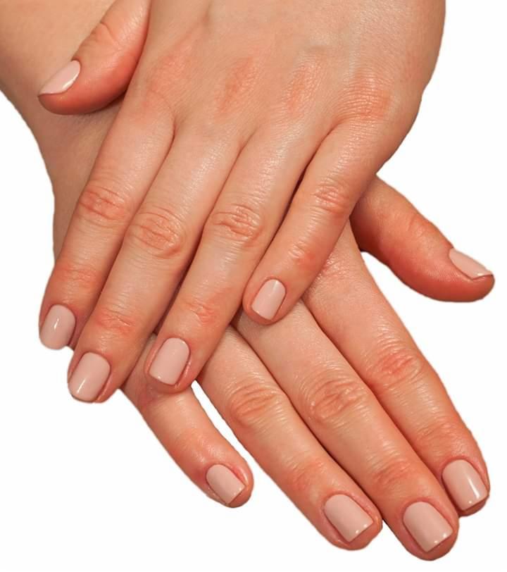 Dłonie kobiety ze świeżo pomalowanymi paznokciami w odcieniu nude, skrzyżowane na białym tle.