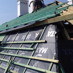 Mirosław Poszelężny - Ekipa dekarzy w trakcie montażu kontrłat na folii paroizolacyjnej dachu, widoczne kominy w tle.