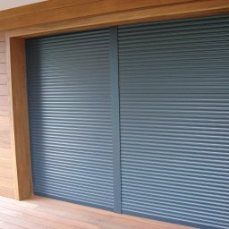 Mirosław Poszelężny - Zewnętrzne rolety antywłamaniowe w kolorze grafitowym, zamontowane na elewacji obłożonej drewnianymi panelami, widoczne z poziomu tarasu.