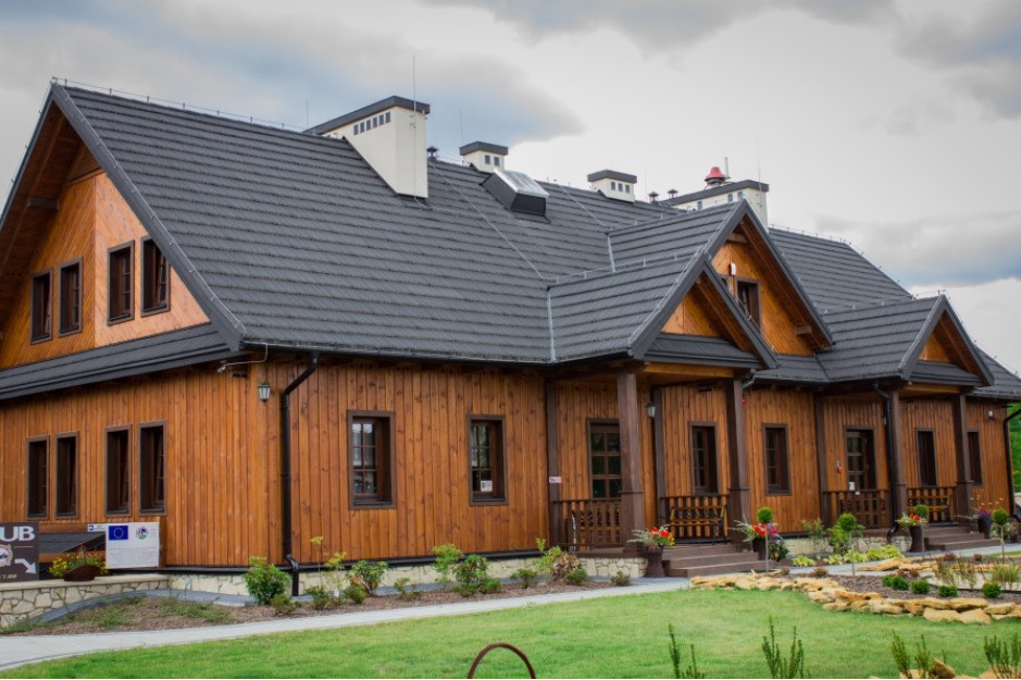 Nowoczesny dom z drewnianą elewacją i grafitowym dachem w Zamościu, widok na front budynku z zadbanym trawnikiem i elementami dekoracyjnymi.