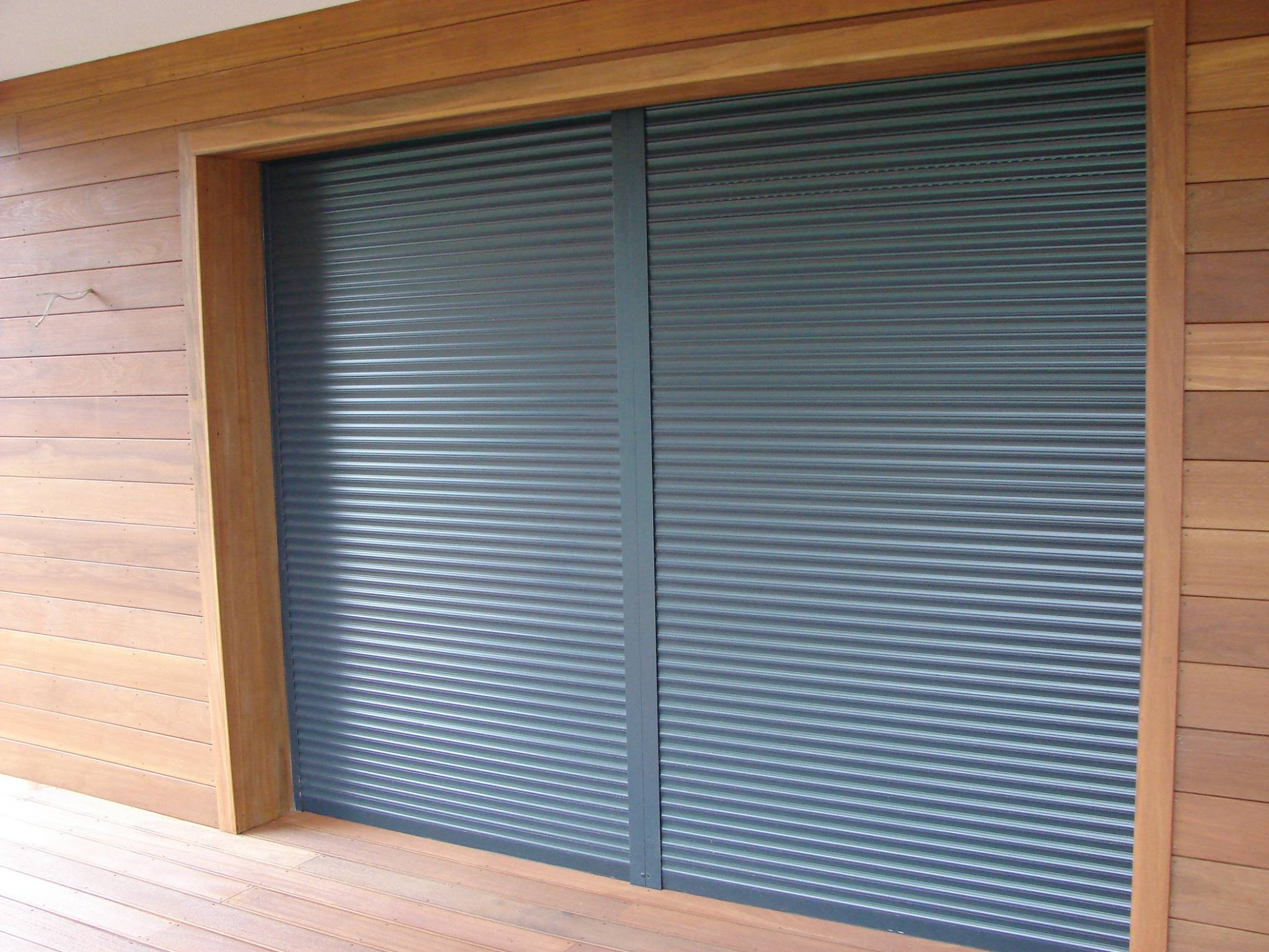 Zewnętrzne rolety antywłamaniowe w kolorze grafitowym, zamontowane na elewacji obłożonej drewnianymi panelami, widoczne z poziomu tarasu.