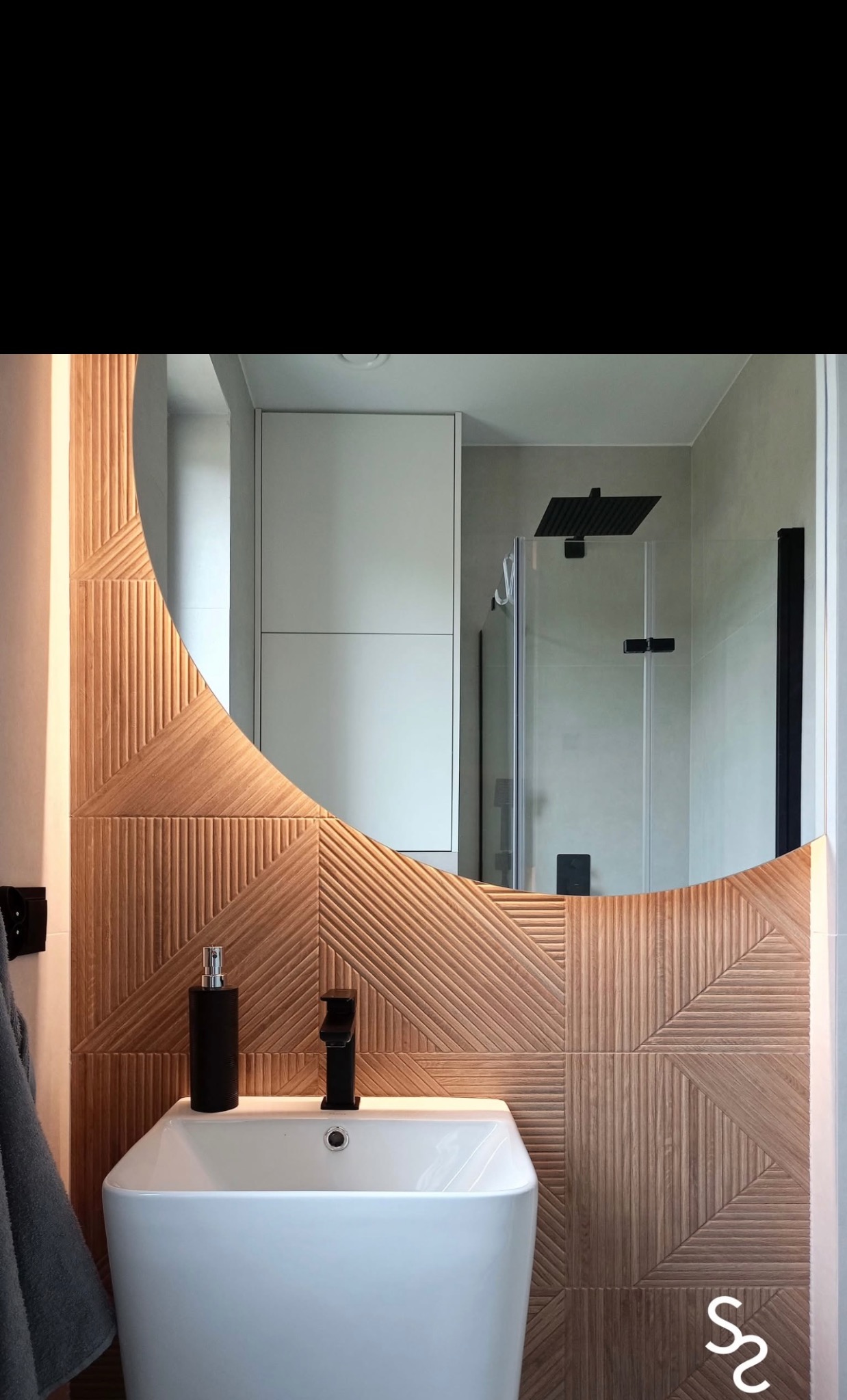 Nowoczesna łazienka z umywalką nablatową i dekoracyjnymi, drewnopodobnymi płytkami ułożonymi w geometryczny wzór. Czarne akcenty armatury i dozownika.