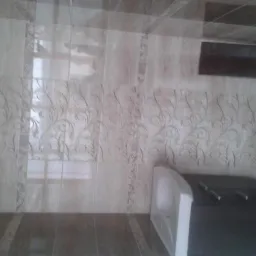 Ściana łazienki wyłożona beżowymi płytkami z delikatnym, roślinnym wzorem, widoczny fragment wanny i zabudowa, ciemna wentylacja na górze.