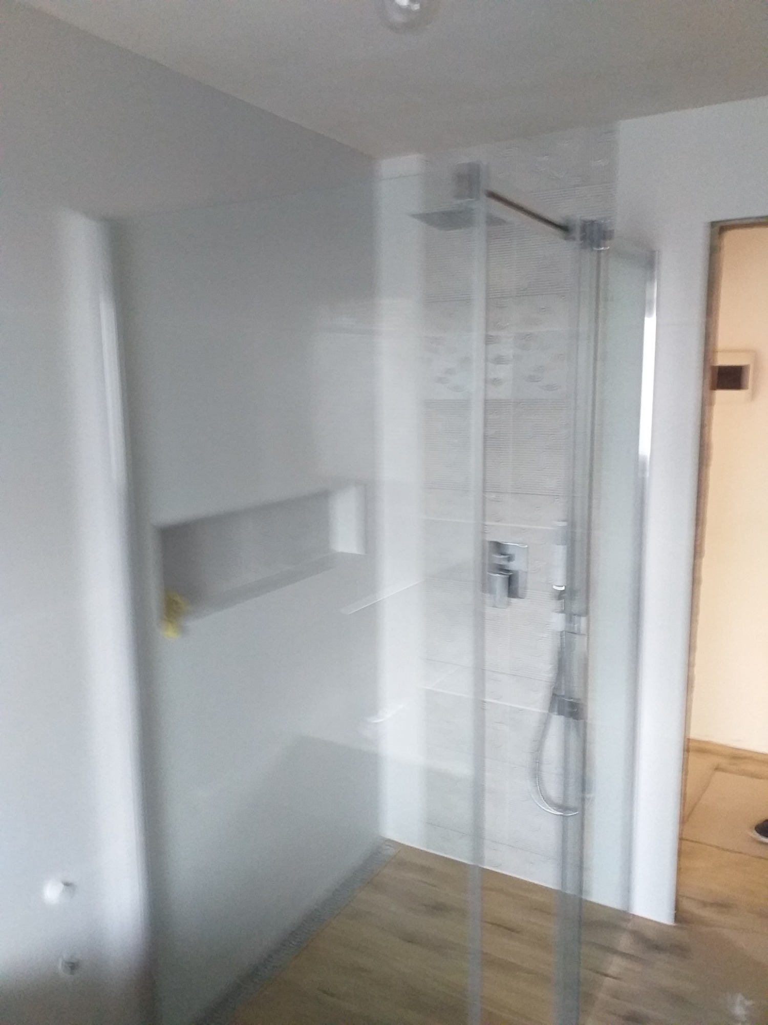 Nowoczesna kabina prysznicowa walk-in z szklaną ścianą i deszczownicą w łazience w Stużno-Kolonia, widok na półkę w ścianie i drewnopodobną podłogę.