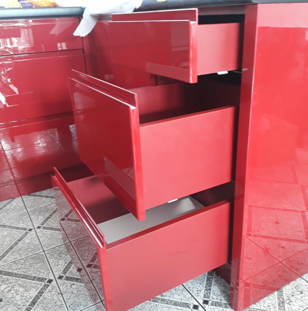 Czerwona szafka kuchenna na wymiar z trzema wysuniętymi szufladami, widoczne wnętrza szuflad w kolorze białym, na podłodze płytki w szaro-białą kratę.