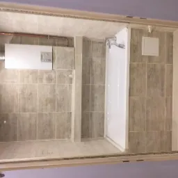 Wykończona łazienka z beżowymi płytkami, białą wanną i zamontowanym piecem gazowym z odprowadzeniem spalin.