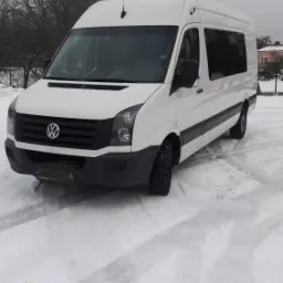 Biały bus Volkswagen Crafter na ośnieżonym terenie w pochmurny dzień, widoczny z przodu pod lekkim kątem.