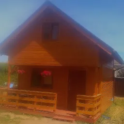 Gotowy, mały, drewniany dom z zadaszonym tarasem, ozdobiony wiszącymi czerwonymi kwiatami, widok z przodu w słoneczny dzień.