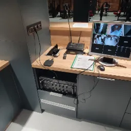 Monitoring wizyjny: Ekran Samsung wyświetlający obraz z kamer Dahua, centrala sterująca i okablowanie zainstalowane w szafce w pomieszczeniu z elementami siłowni w tle.