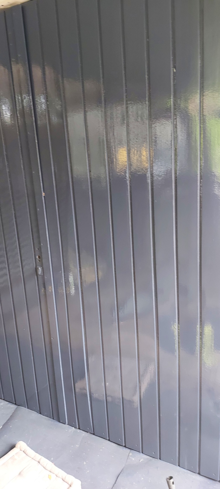 Świeżo pomalowana, błyszcząca, szara elewacja z pionowych paneli, widoczne odbicia światła i niewielkie niedoskonałości malowania przy krawędziach.