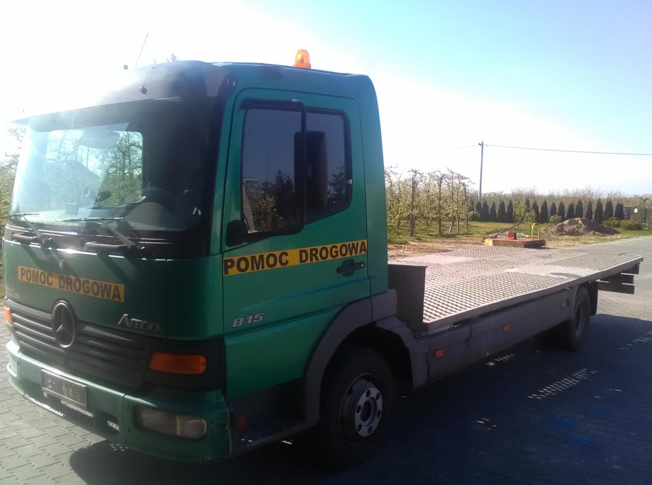 Zielona laweta Mercedes Atco 815 z napisem 'Pomoc Drogowa' na tle sadu owocowego w słoneczny dzień.