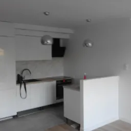 Nowoczesna, minimalistyczna kuchnia z białymi szafkami, marmurowym backsplashiem i srebrnymi lampami wiszącymi. Widoczny czarny zlew z baterią i płyta indukcyjna. Świeżo wyremontowane wnętrze...