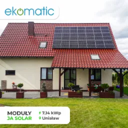 Dom jednorodzinny z czerwoną dachówką i panelami fotowoltaicznymi na dachu, widok z ogrodu z trawnikiem i ozdobnymi roślinami w donicach, moduły JA Solar i moc 7,14 kWp.
