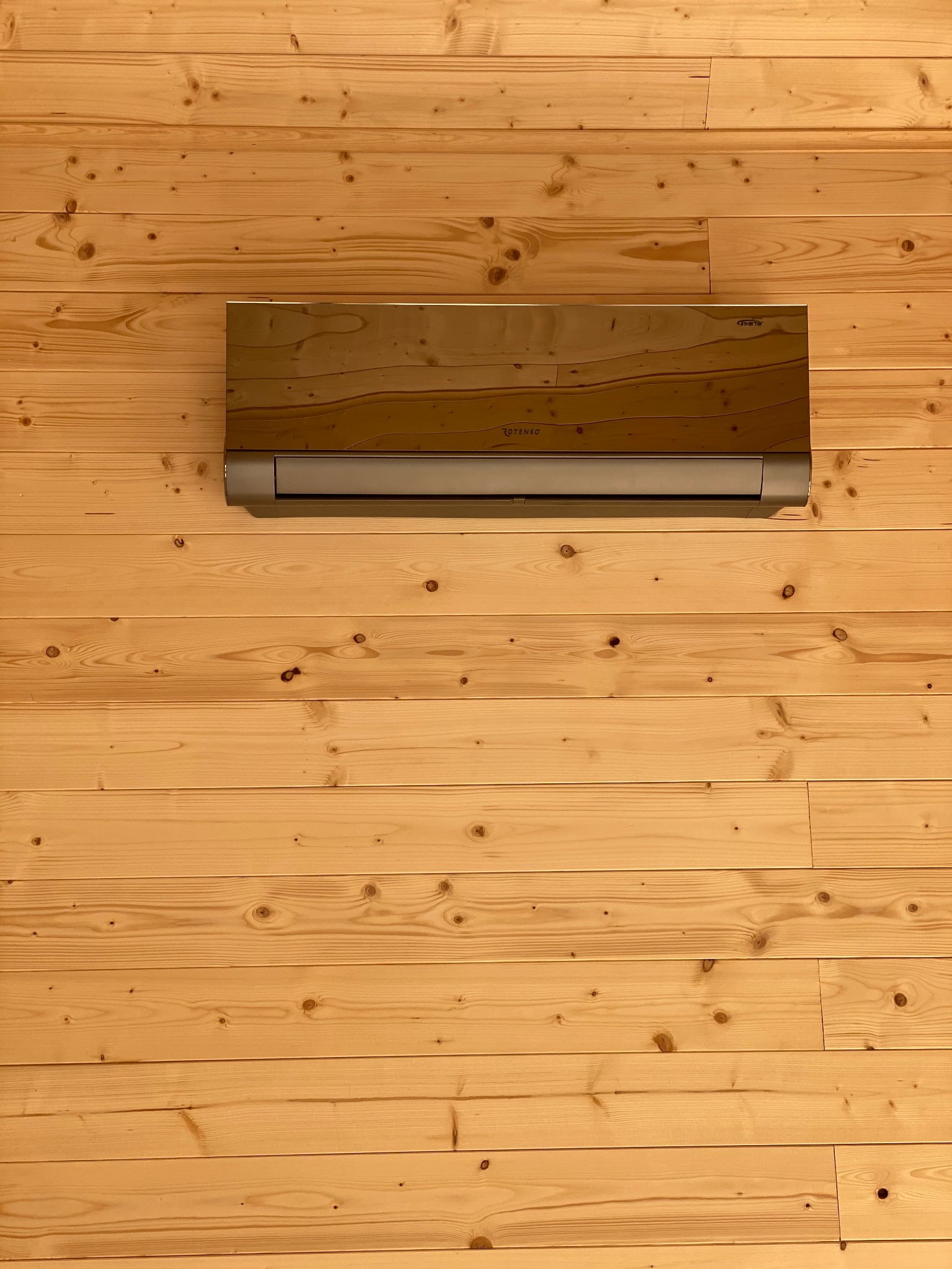 Klimatyzator marki Rotenso zamontowany na ścianie wyłożonej jasnym drewnem w stylu skandynawskim.