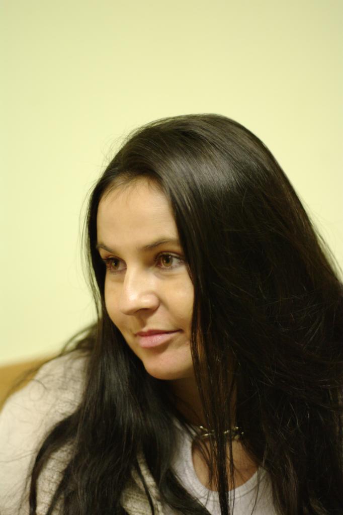 Portret kobiety z długimi, ciemnymi włosami, patrzącej w bok na tle jasnej ściany w Dąbrowie Górniczej.