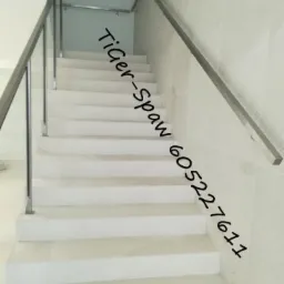 Białe schody z zamontowaną metalową poręczą po prawej stronie i balustradą po lewej, widok z dołu.