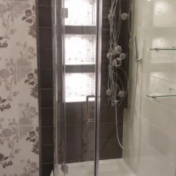 Nowoczesna kabina prysznicowa z hydromasażem, szklane półki, wzorzyste płytki na ścianie, widoczne detale wykończenia.